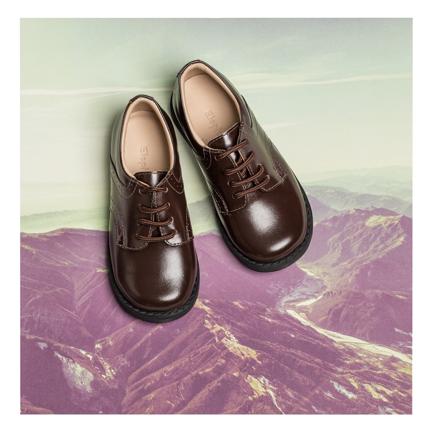 Toddler brown leather lace-up shoes with rounded toes and cushioned insoles on a scenic background.
