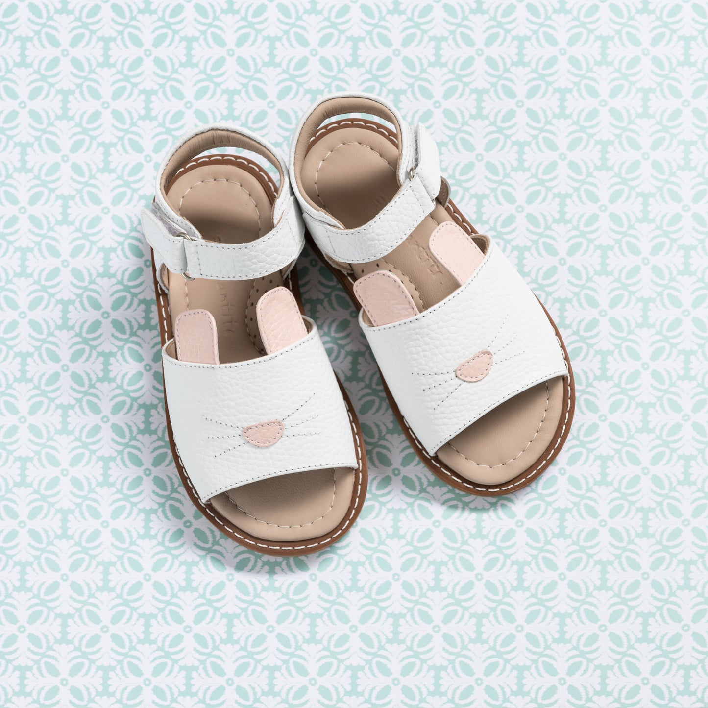White leather toddler sandals with bunny cutout and brown cushioned sole on patterned surface.