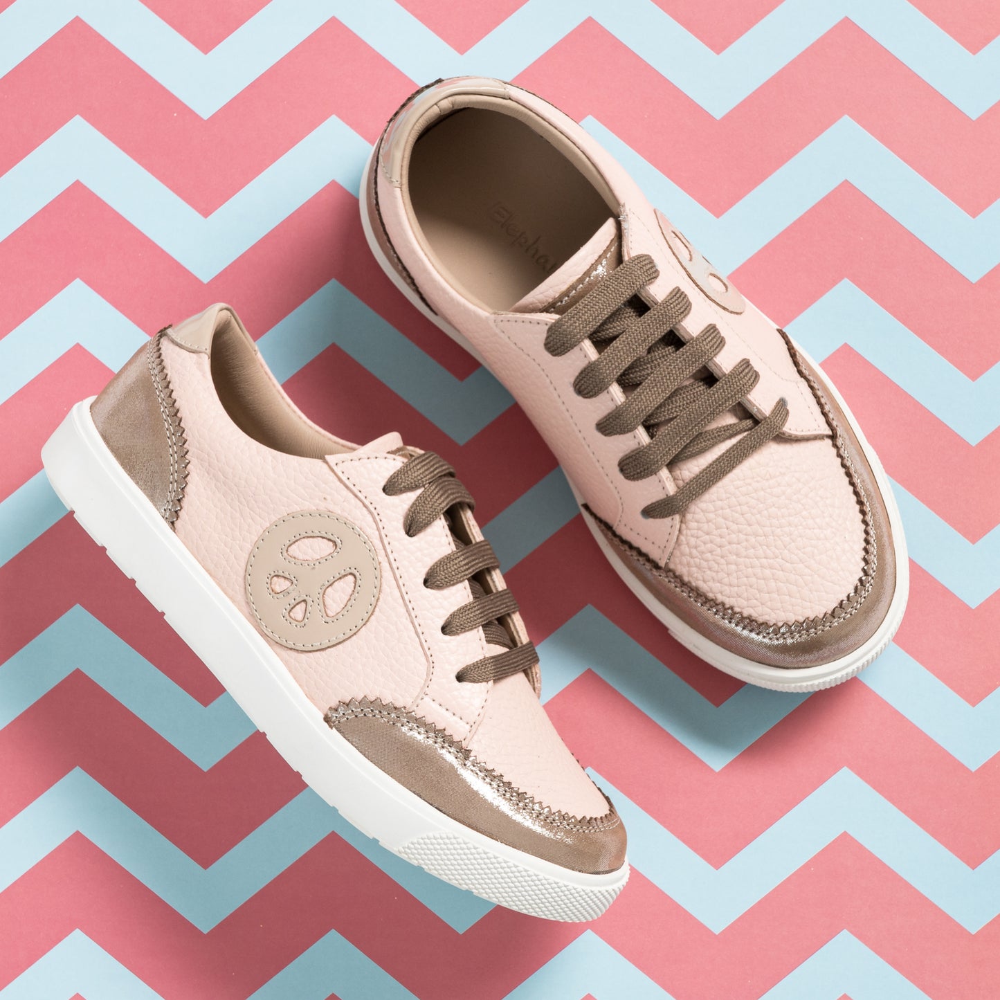 Pink textured girls' sneakers with beige accents, brown laces, and white soles on zigzag background.
