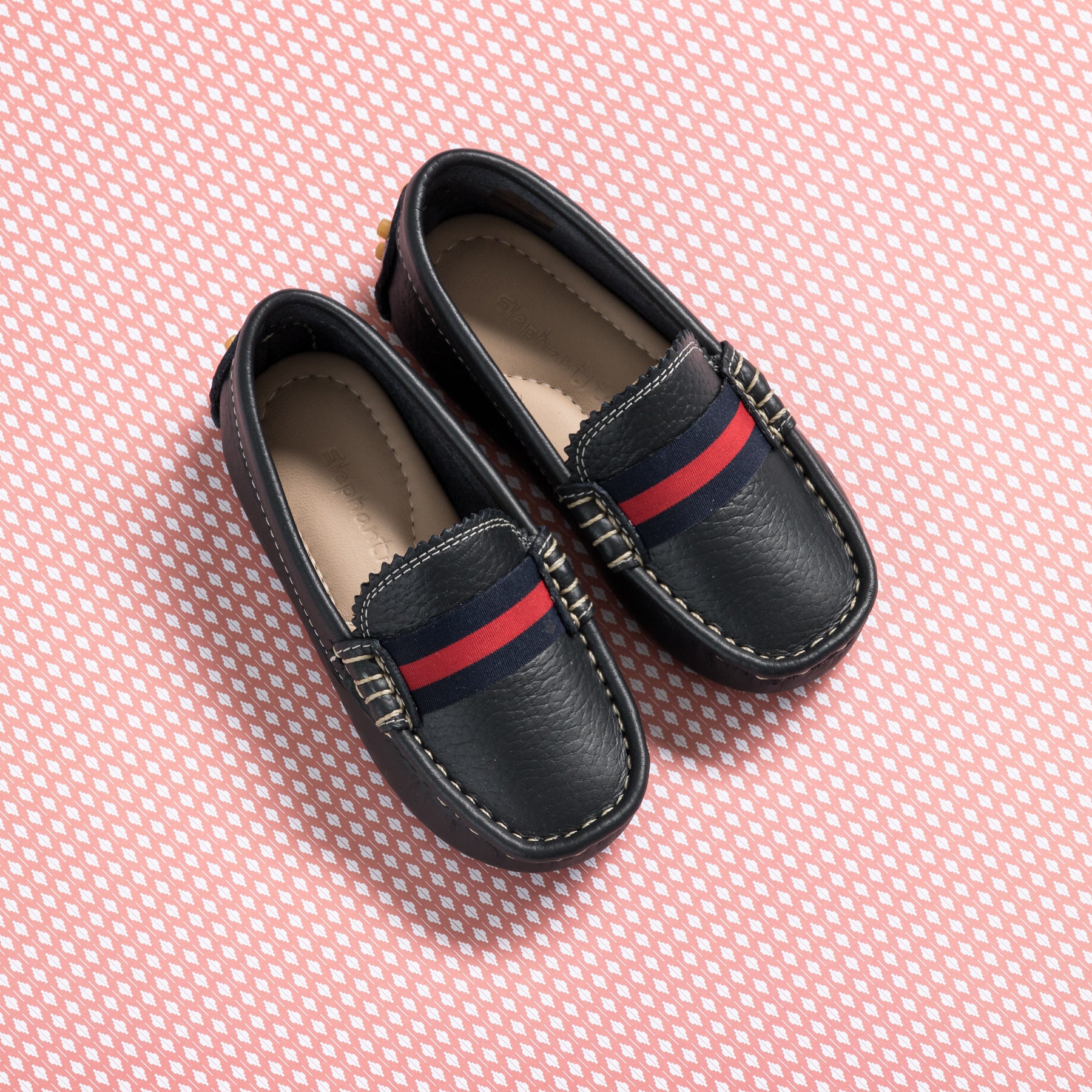 Navy blue boys’ loafers with red and blue striped strap and white stitched detailing.
