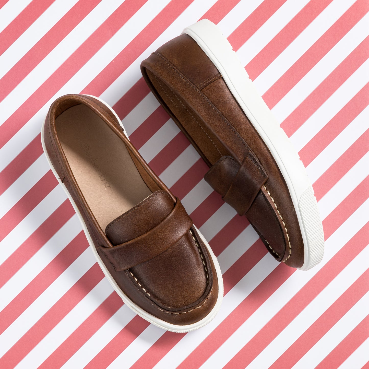 Brown leather boys' loafers with white rubber soles and moccasin-style stitching.