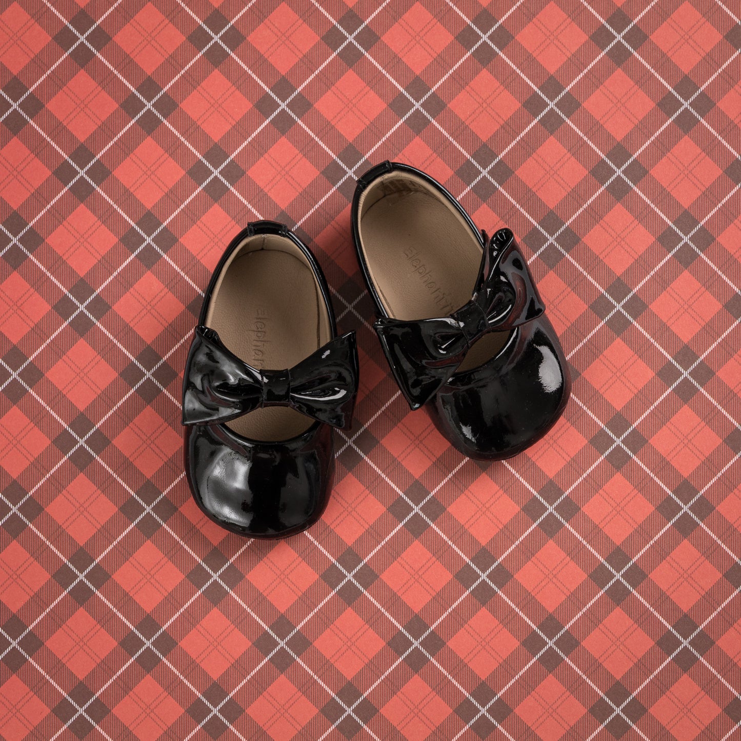 Glossy black patent leather baby ballerina shoes with decorative bows on top.