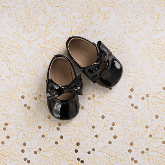 Glossy black patent leather baby ballerina shoes with decorative bows on top.
