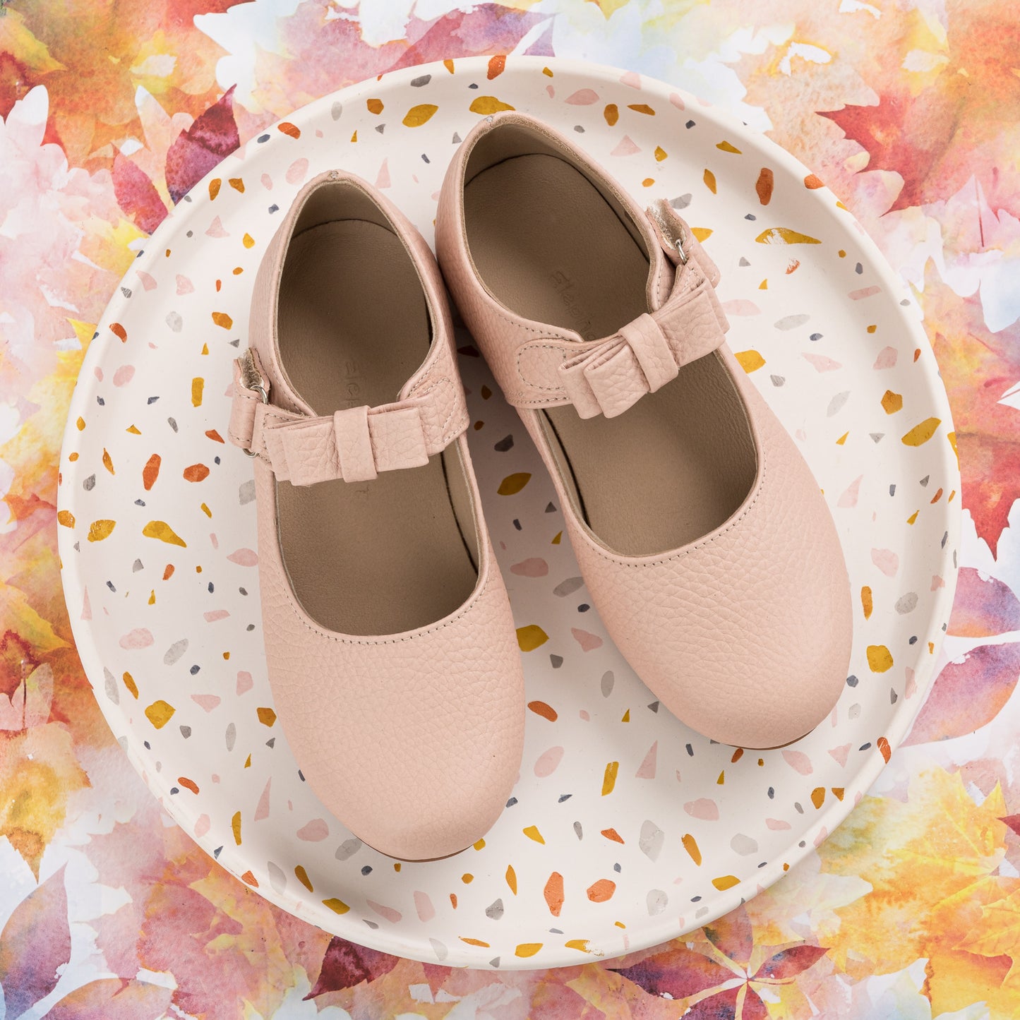 Pink toddler Mary Jane shoes with textured finish and bow strap on terrazzo plate.