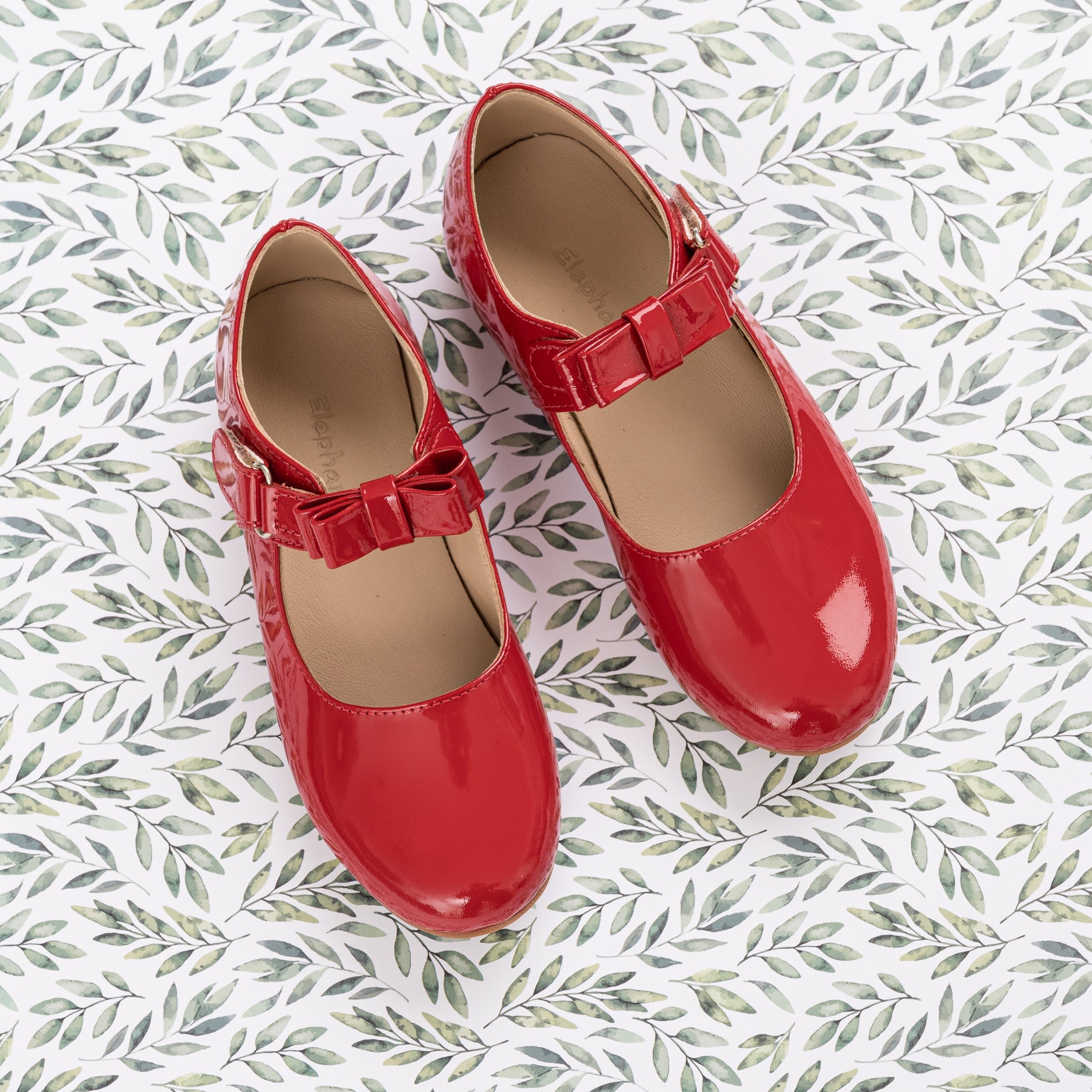 Glossy red patent leather Mary Jane shoes with bow detail and hook-and-loop strap for kids.