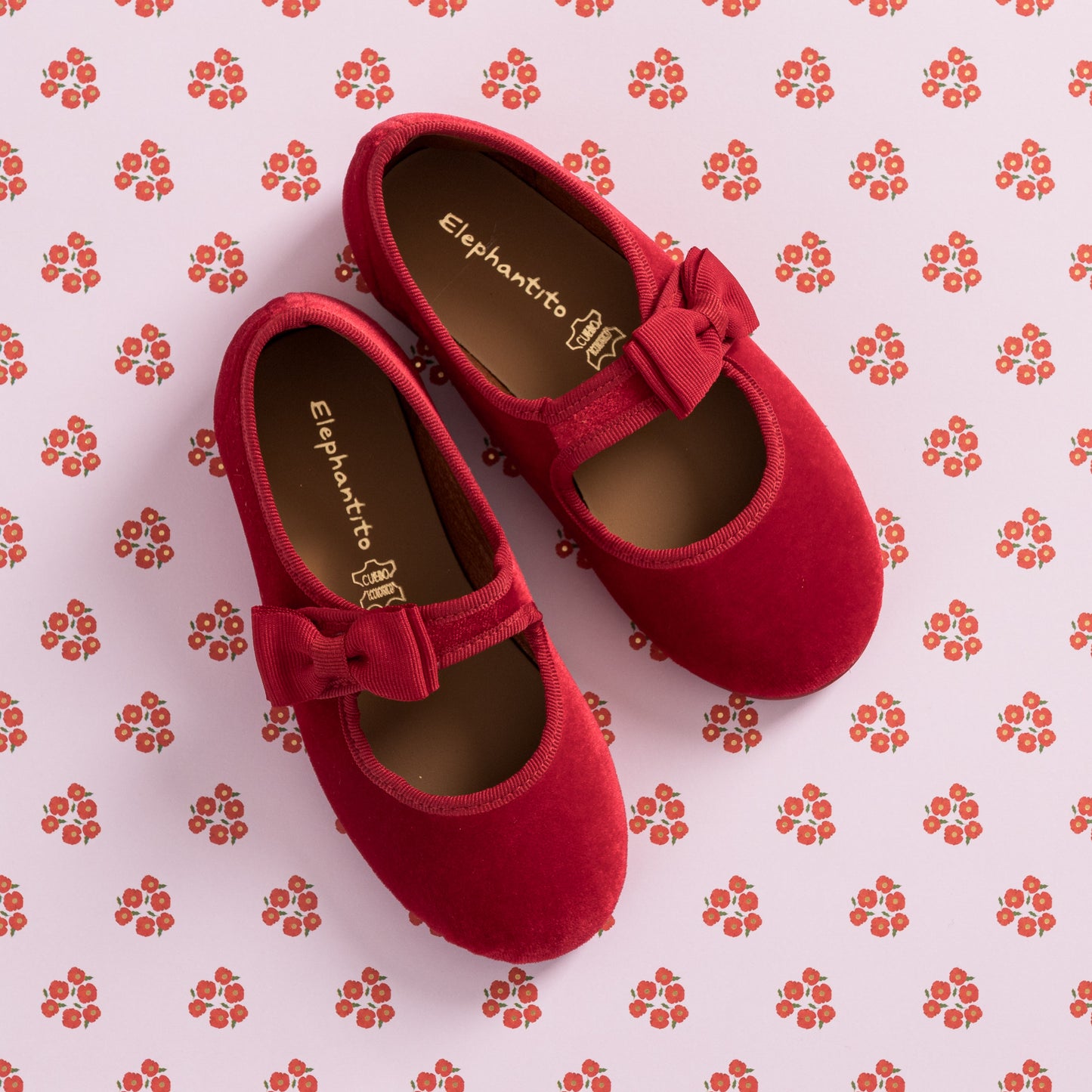 Red velvet toddler Mary Jane shoes with bow detail and brown cushioned insoles on patterned background.