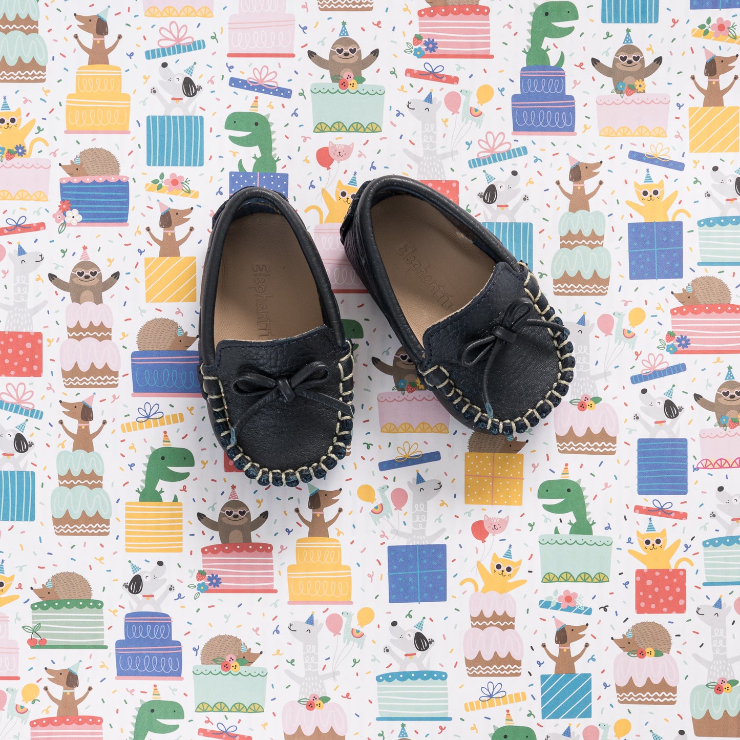 Navy blue baby driver loafers with bow detail and stitched trim on playful patterned background.