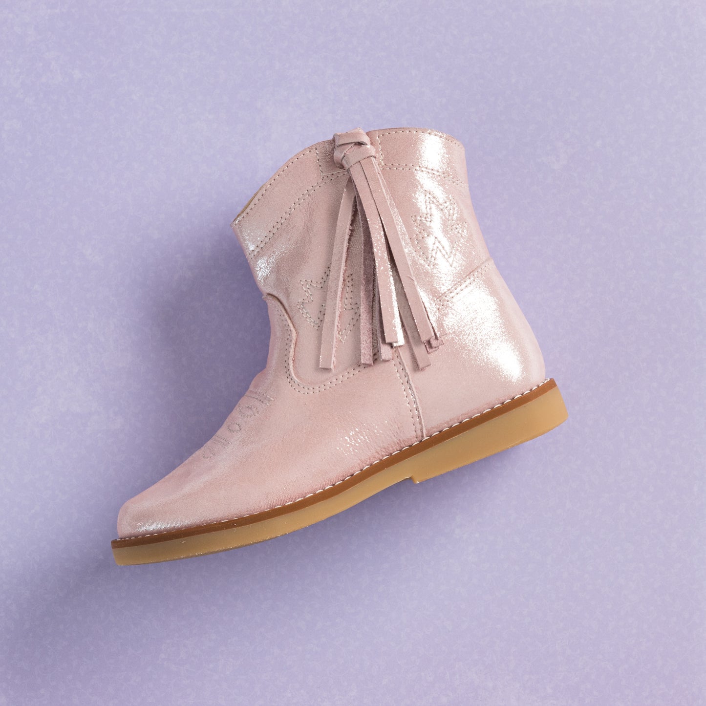 Metallic pink suede toddler boot with tassel detail and light brown sole on lavender background.