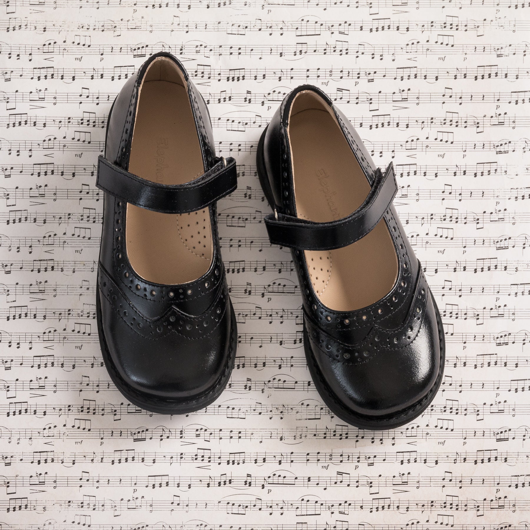 Black leather Mary Jane shoes for girls with perforated brogue details and adjustable straps.