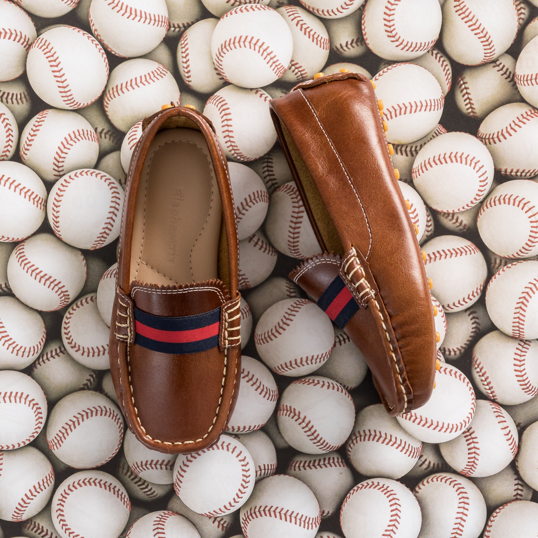Natural brown leather baby loafers with navy and red striped elastic band, moccasin stitching.