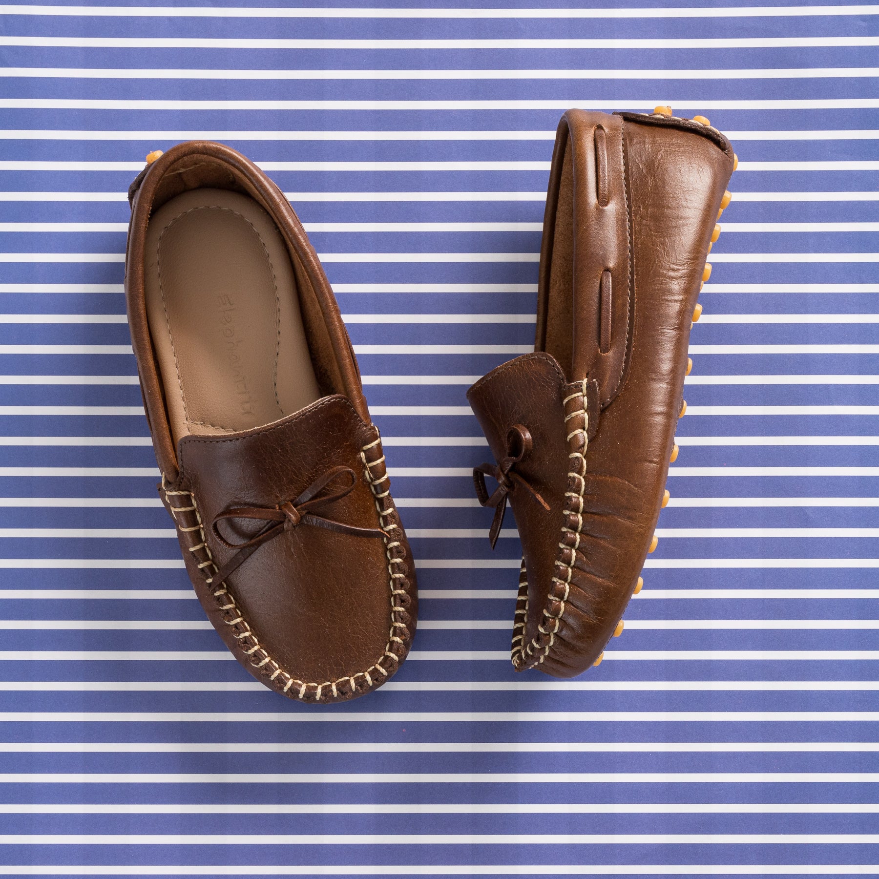 Brown leather driver loafer with stitched trim and decorative bow on top.