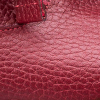 Close-up of red textured leather with pebbled grain and part of stitched bow detail.