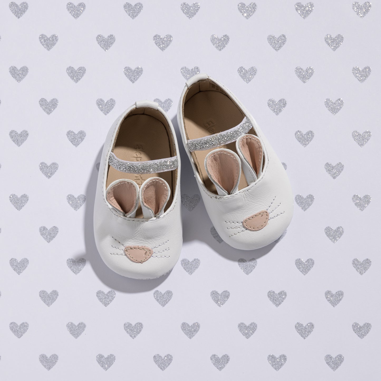 White baby slippers with soft fabric bunny ears and embroidered nose on top.