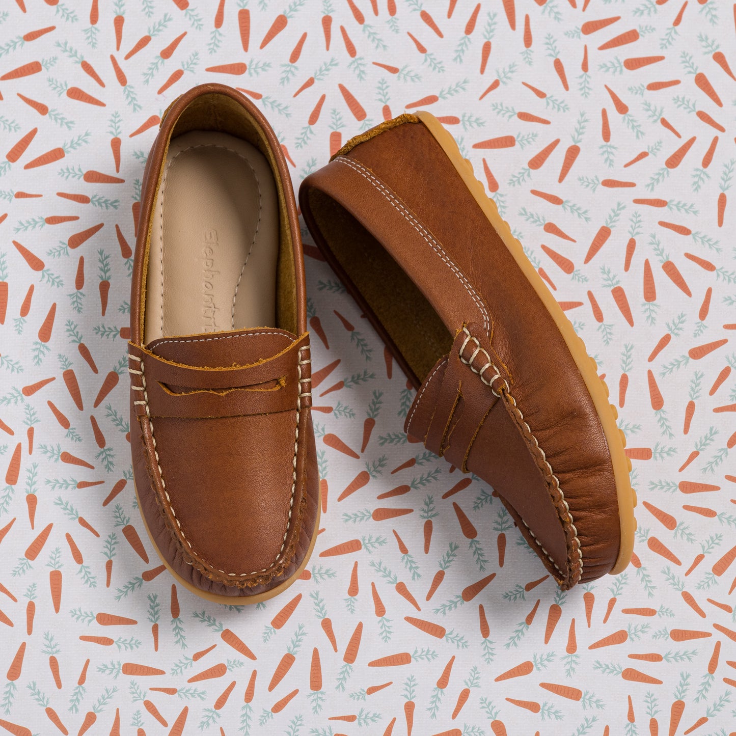 Brown leather moccasin loafers with stitched detailing and soft soles on a patterned background.