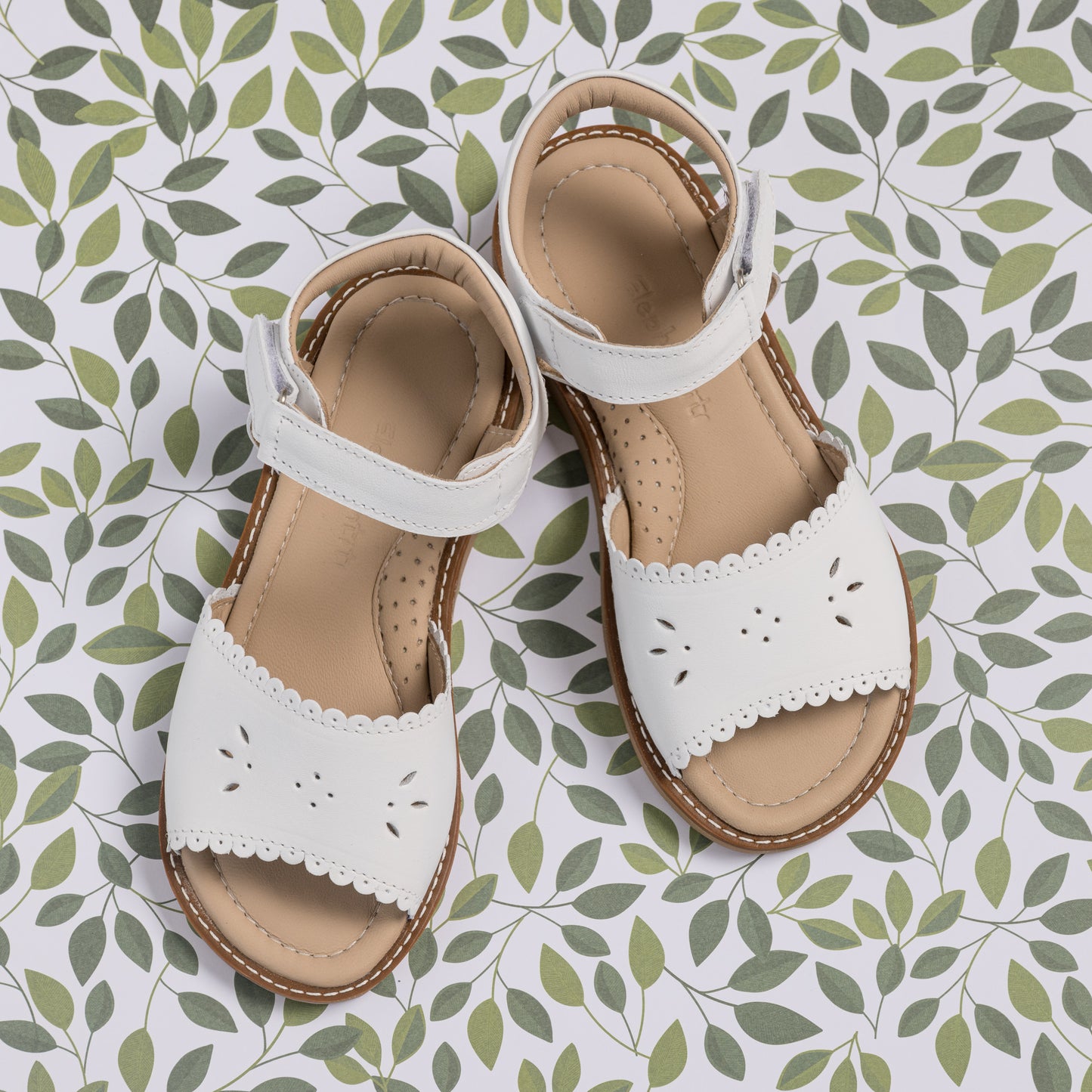 White toddler sandals with scalloped edges and flower cut-out details on tan soles.