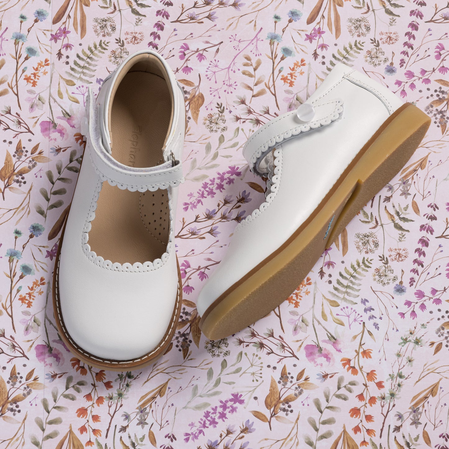 White leather Mary Jane shoes with scalloped edges and velcro strap, tan rubber sole.