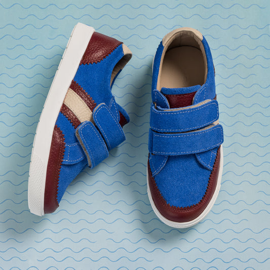 Blue denim boys sneakers with brown leather accents and double velcro straps on white soles.