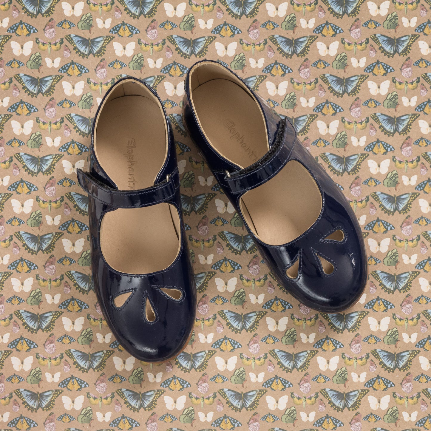 Navy blue patent leather girls Mary Jane shoes with teardrop cutouts and a strap buckle closure.