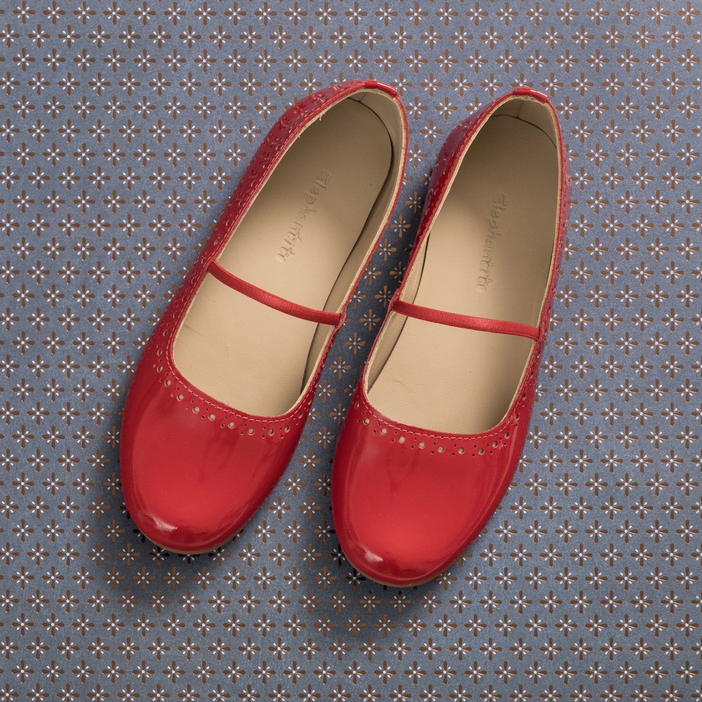 Red patent leather ballerina flats with a thin strap and perforated detailing around the toe.