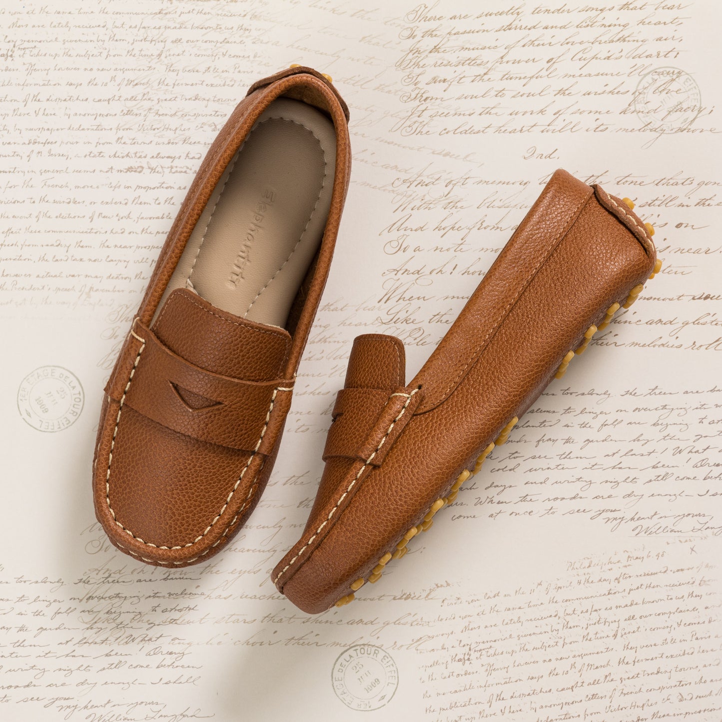 Tan leather children's loafer with stitched detailing and rubber grip sole on beige background.