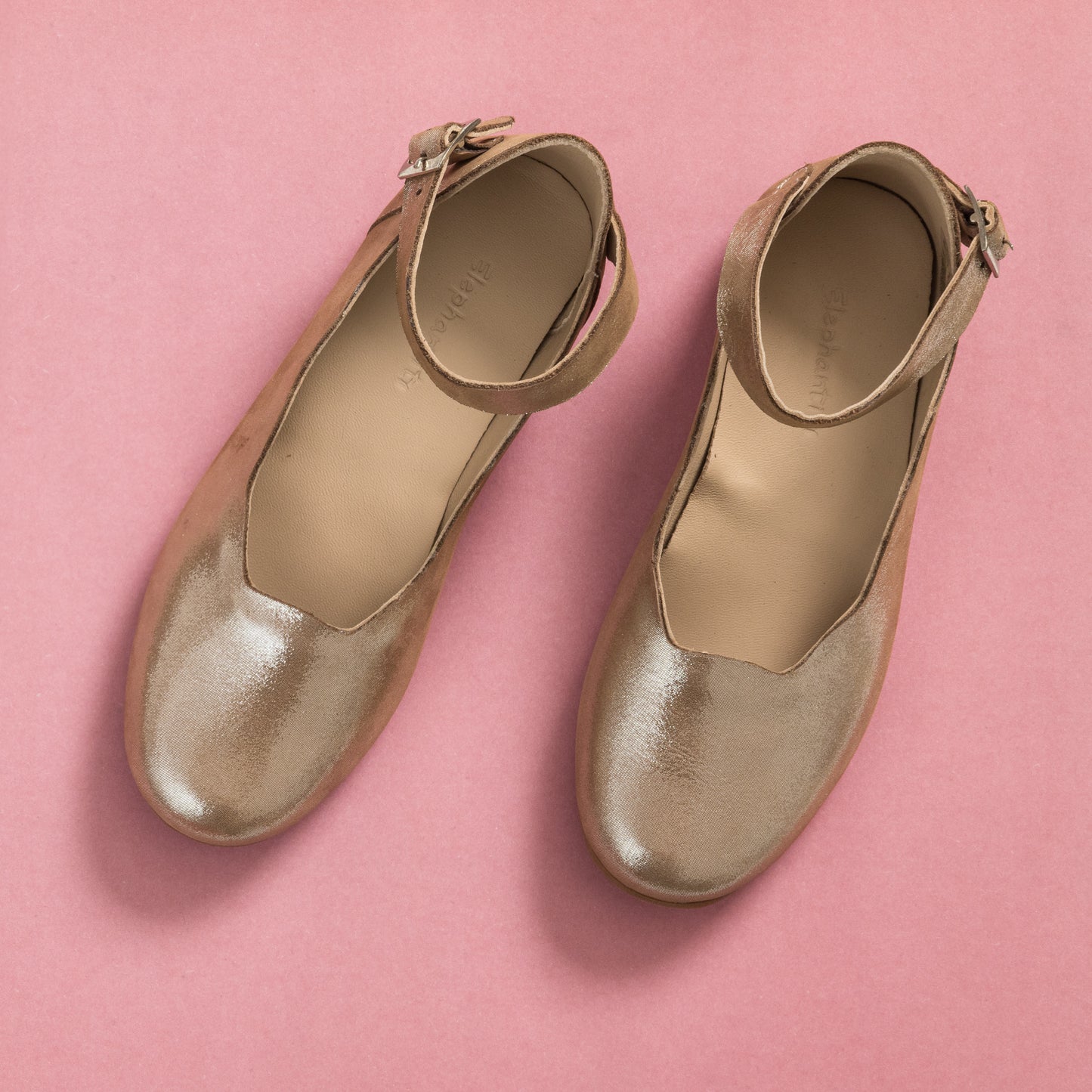 Blush pink toddler flats with ankle straps and shiny finish on a pink background.