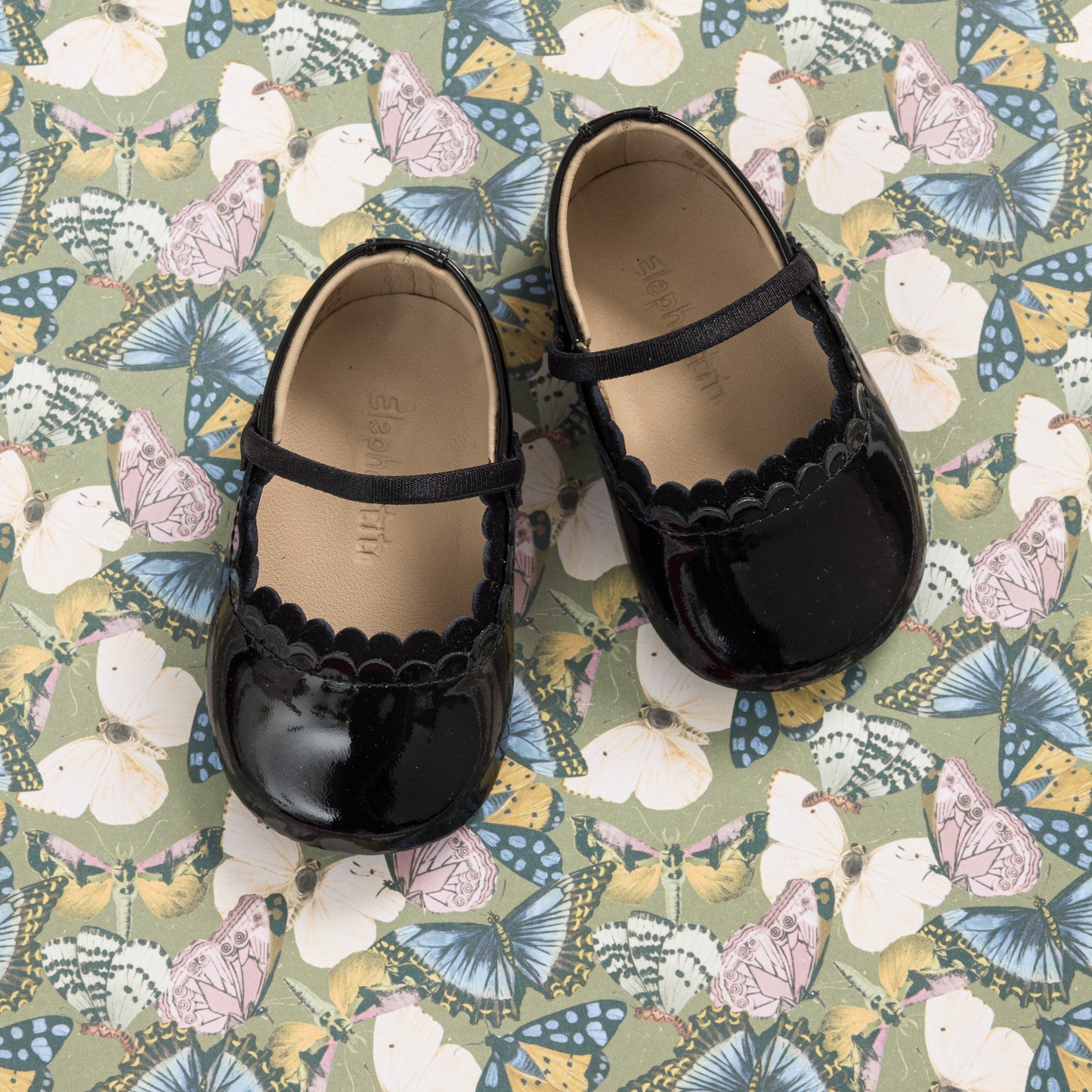 Glossy black patent baby ballet shoes with scalloped edge and a slim strap over the instep.
