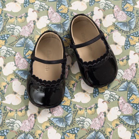 Glossy black patent baby ballet shoes with scalloped edge and a slim strap over the instep.