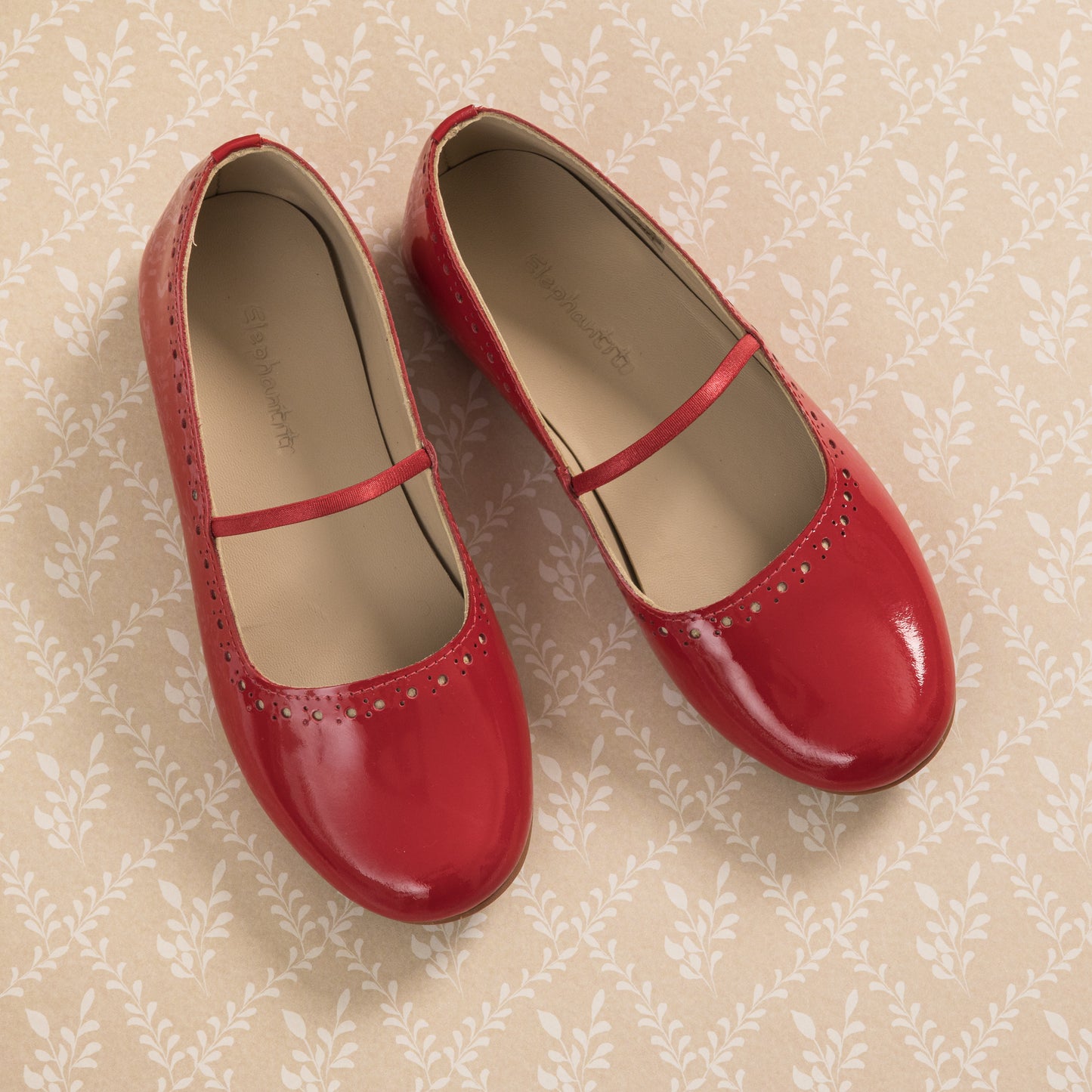 Red patent leather ballerina flats for girls with a thin strap and perforated detailing near the toe.