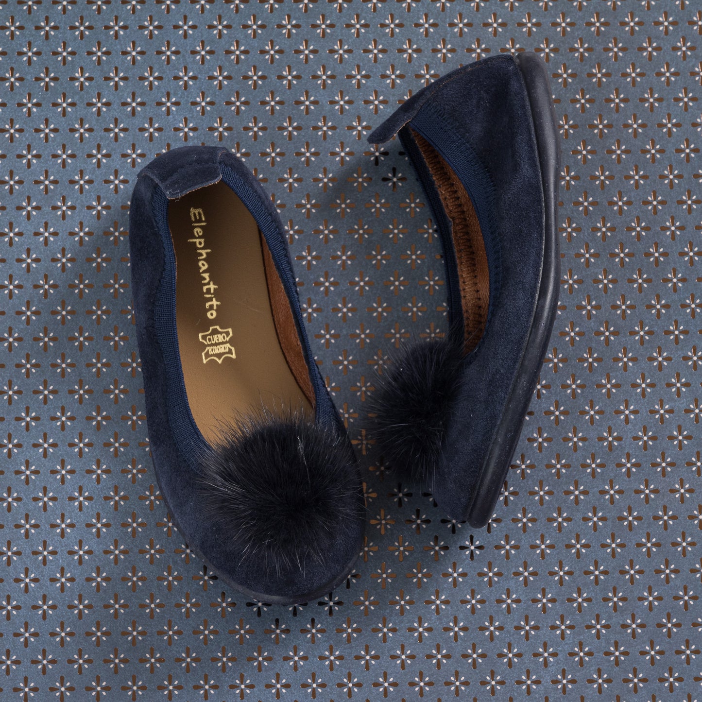 Navy blue suede ballerina shoes with fluffy pom pom on top and rounded toe for kids.