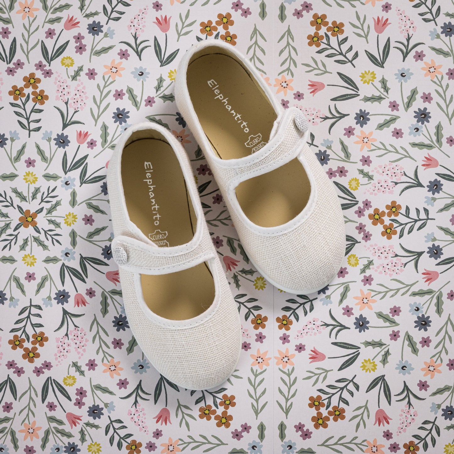 White linen Mary Jane toddler shoes with single strap and round toe on floral background.