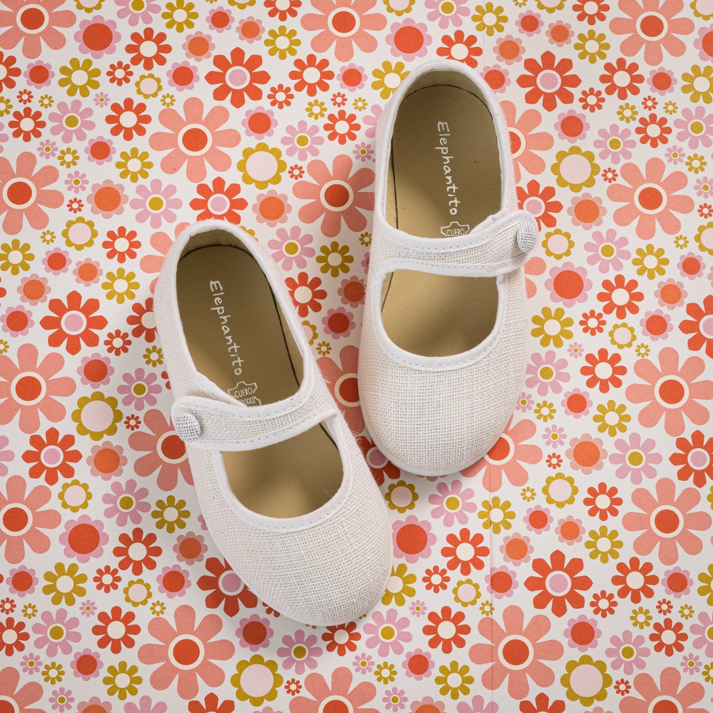 White linen toddler Mary Jane shoes with button strap on colorful floral background.