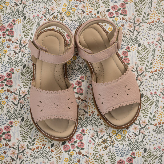 Pink toddler sandals with scalloped edges, perforated floral design, and ankle straps on floral background.