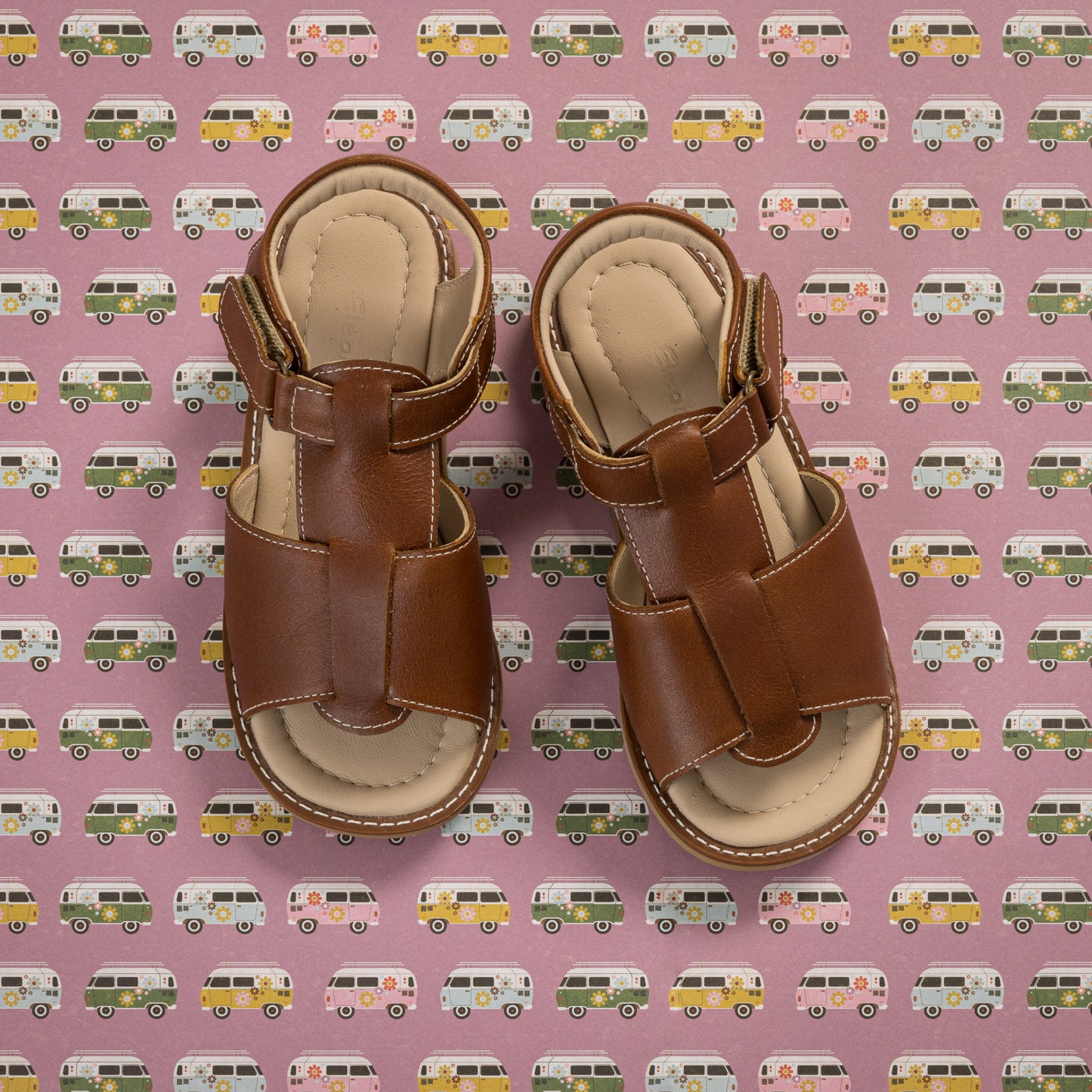 Natural brown leather boy's sandals with adjustable ankle straps and closed heel design on patterned background.