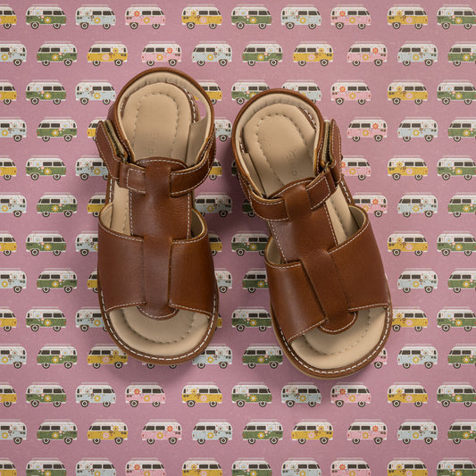 Natural brown leather boy's sandals with adjustable ankle straps and closed heel design on patterned background.