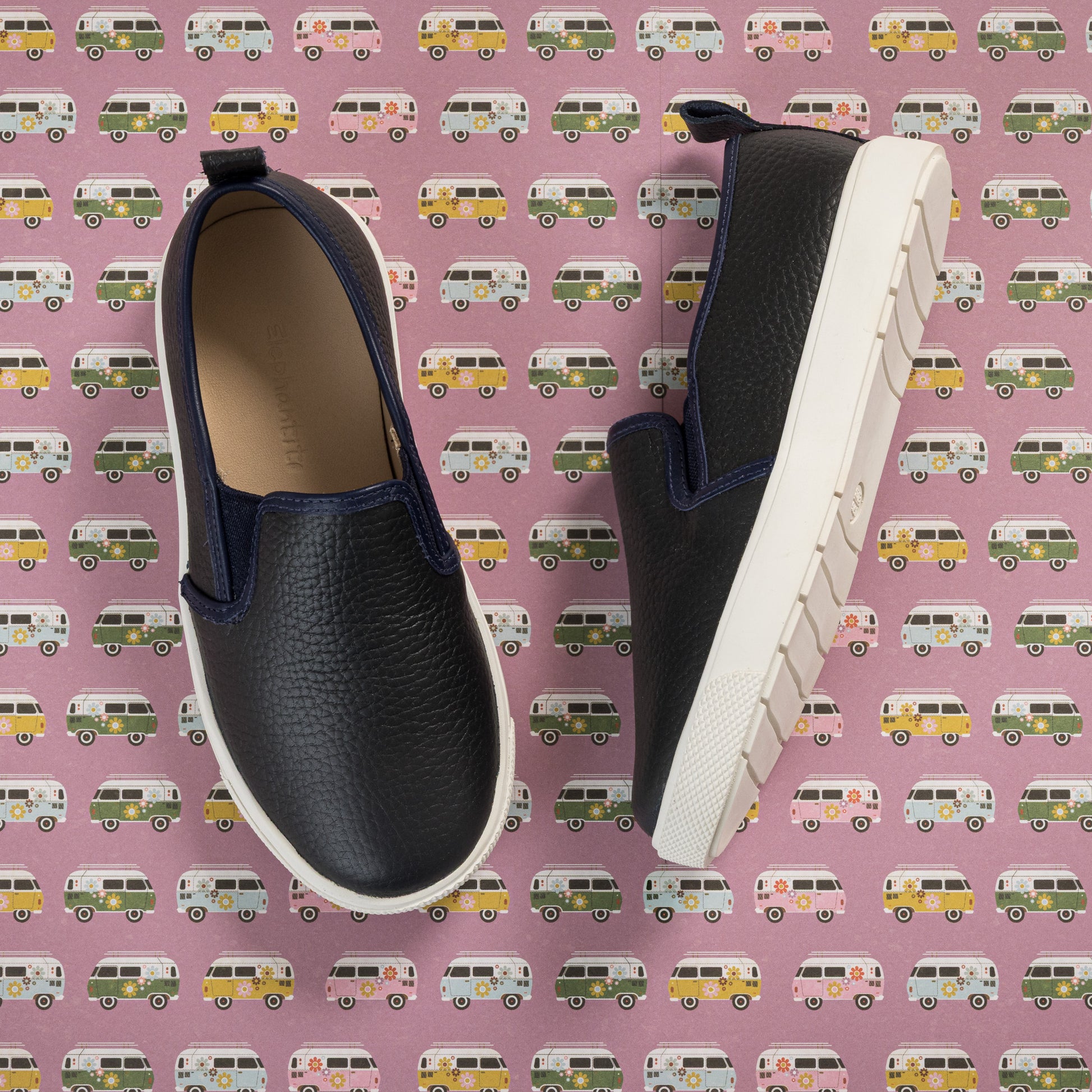 Children's slip-on shoes with textured navy blue upper and thick white sole on patterned background.