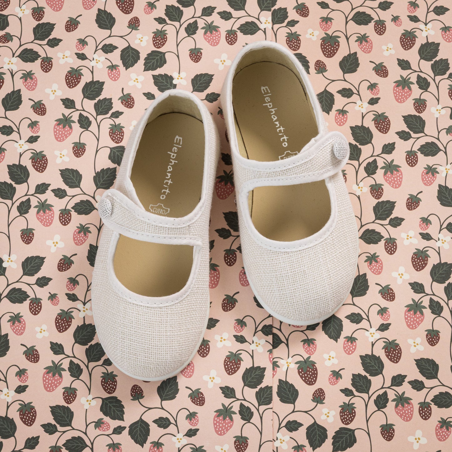 White linen Mary Jane toddler shoes with adjustable strap on floral fabric background.