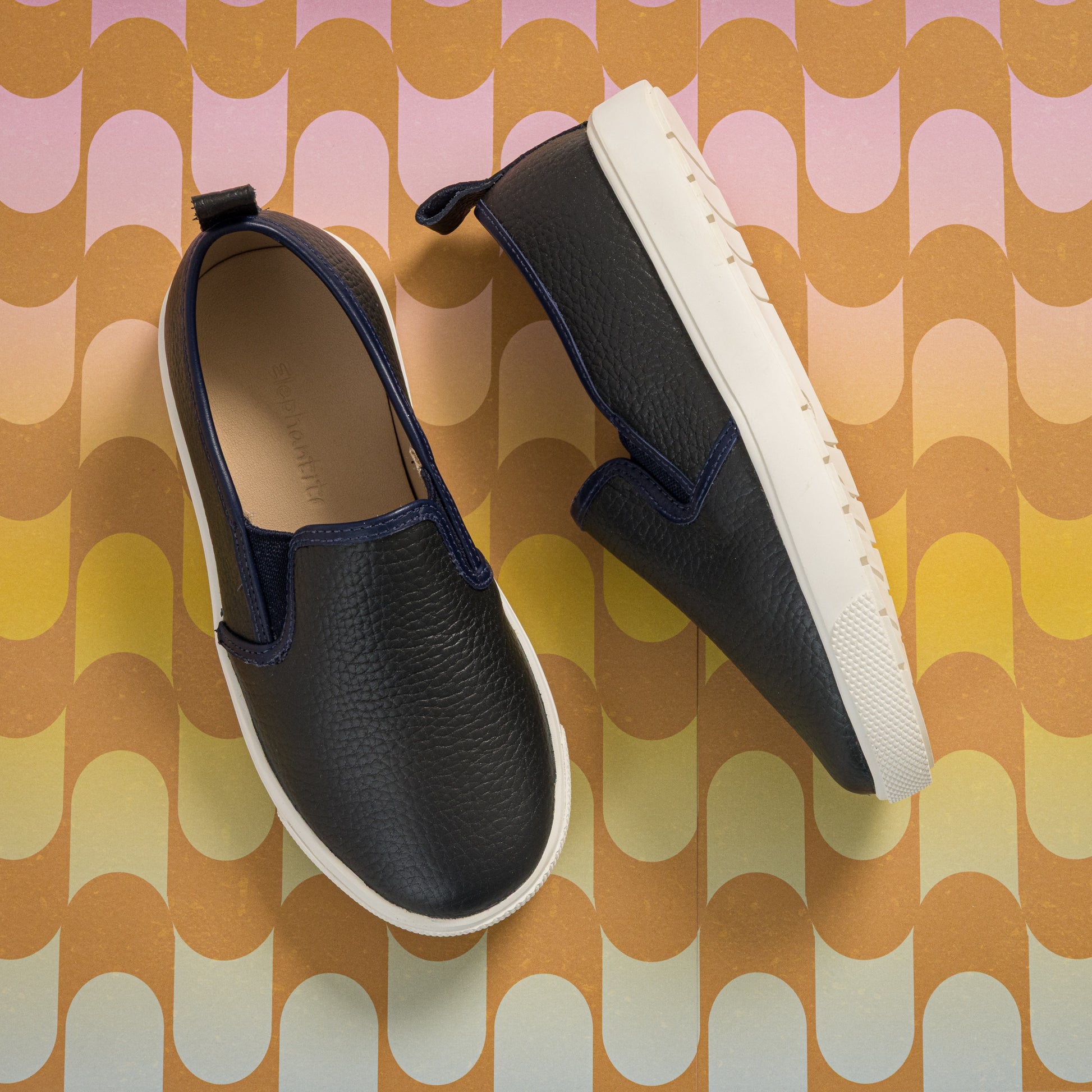 Black textured slip-on shoes for kids with white soles and pull tabs at the heel.