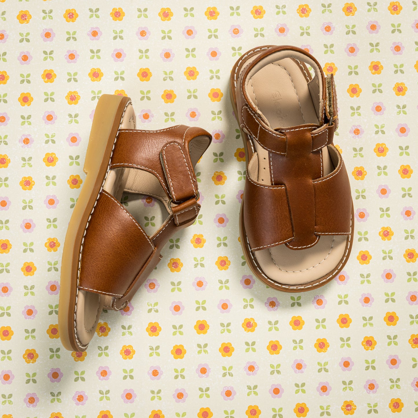 Natural brown leather boy sandal with open toe and velcro strap closure on patterned background.