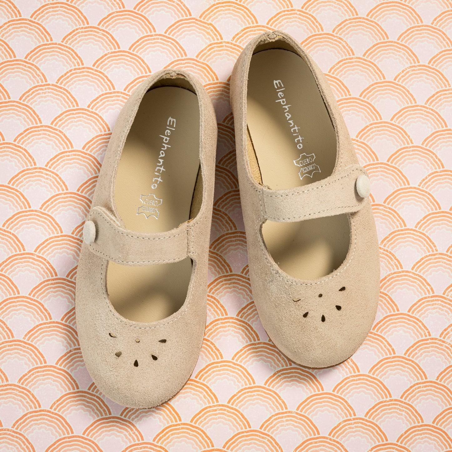 Beige suede toddler Mary Jane shoes with perforated floral design and single strap closure.