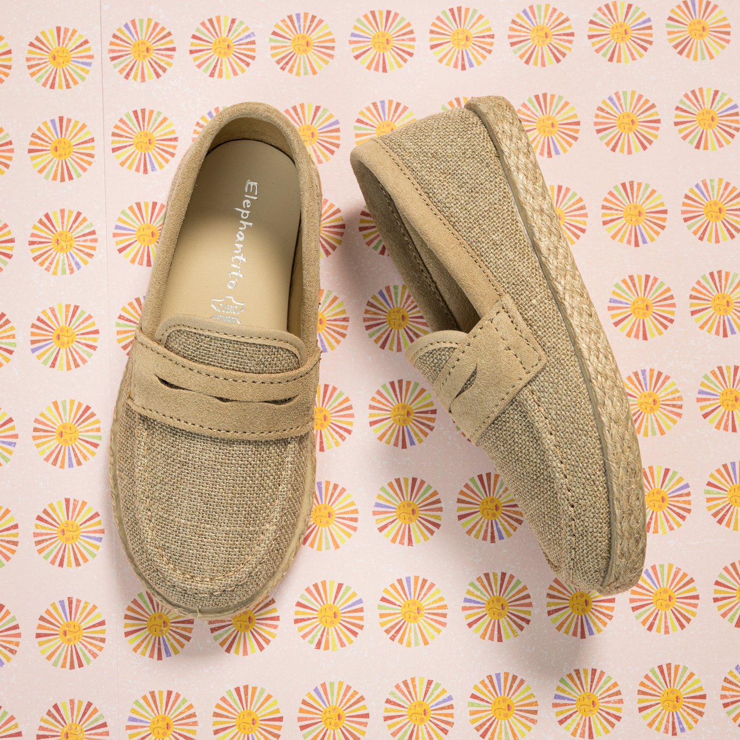 Beige toddler loafer espadrilles with woven jute sole and suede-like upper on floral background.