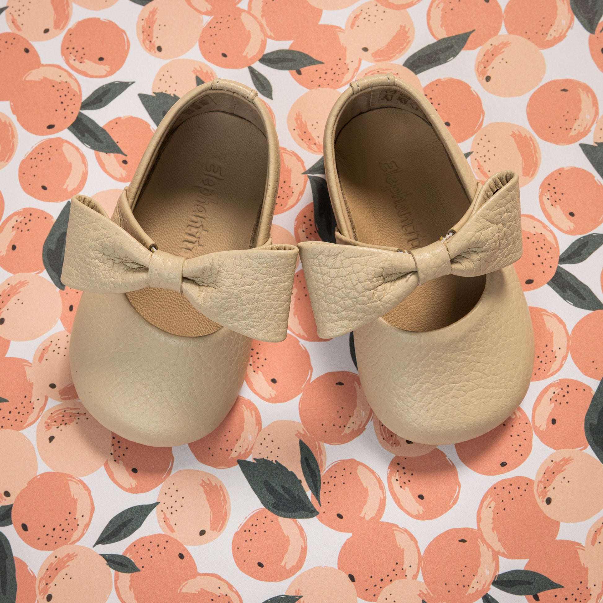 Cream-colored baby ballerina shoes with textured large bows on top and round toes.