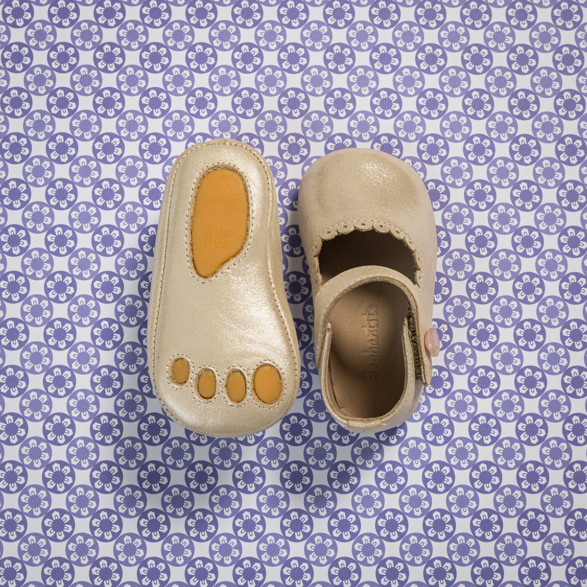 Soft cream-colored baby Mary Jane shoes with scalloped edges and a tan sole patch shaped like toes.