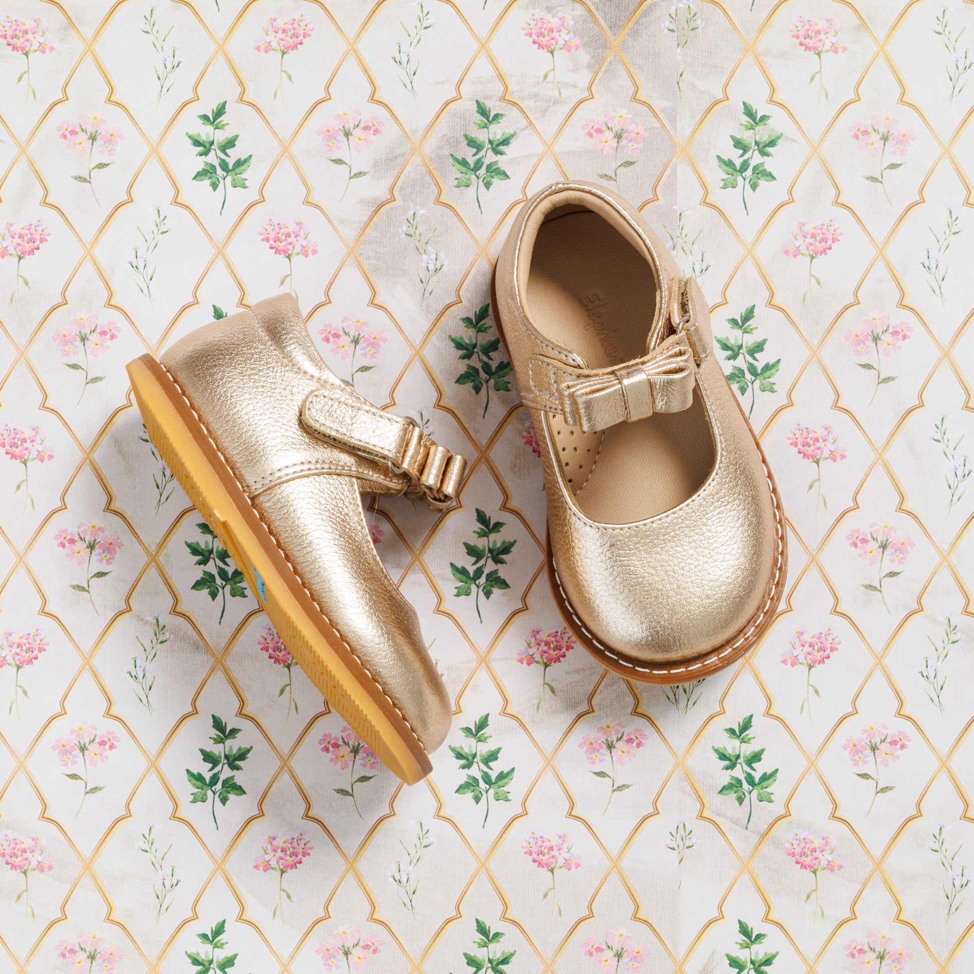 Toddler Mary Jane shoes in metallic gold with a bow detail and brown rubber sole.
