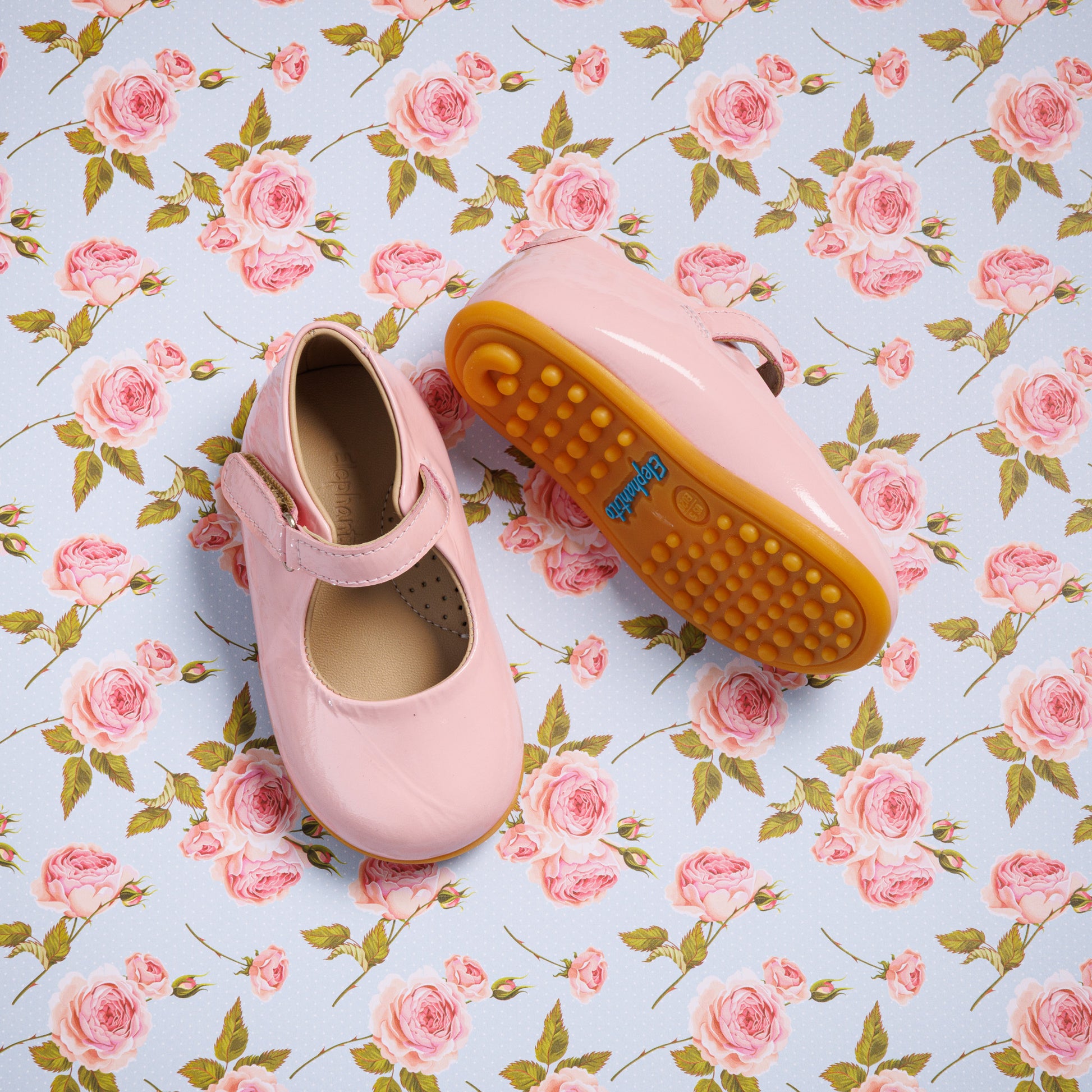 Pink toddler Mary Jane shoes with strap and brown rubber soles on floral background.