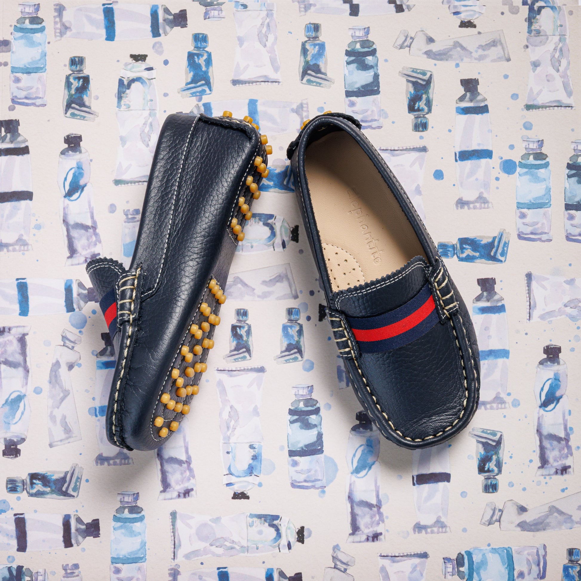 Navy blue boys' leather loafers with red and navy striped detailing and rubber studded soles.