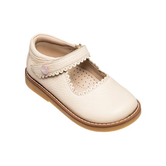 Cream-colored girls Mary Jane shoe with scalloped edges and Velcro strap on brown sole.