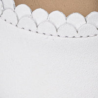 White baby leather shoe with scalloped edge detail and smooth texture.