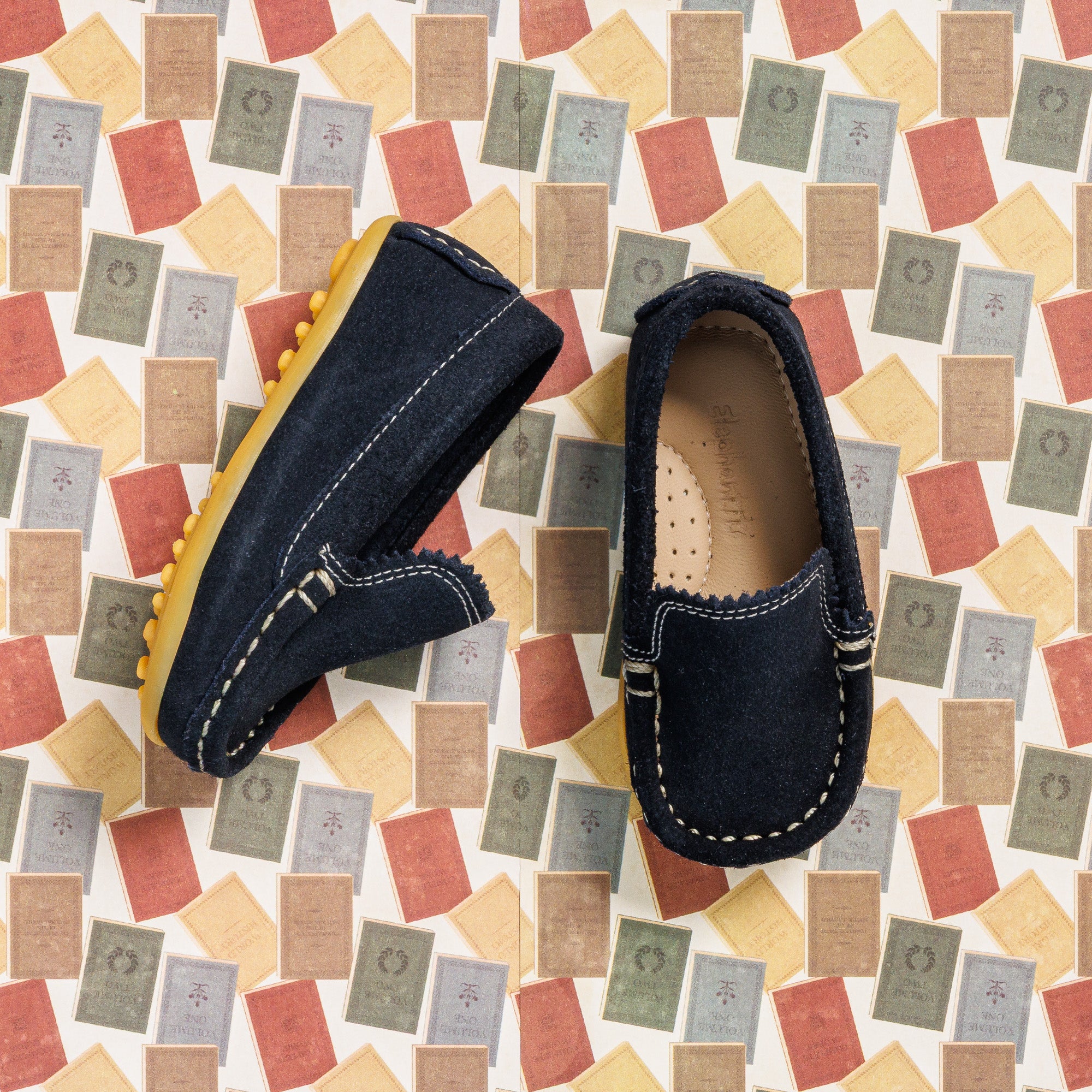 Navy blue suede toddler moccasin shoes with yellow soles and white stitching detail.