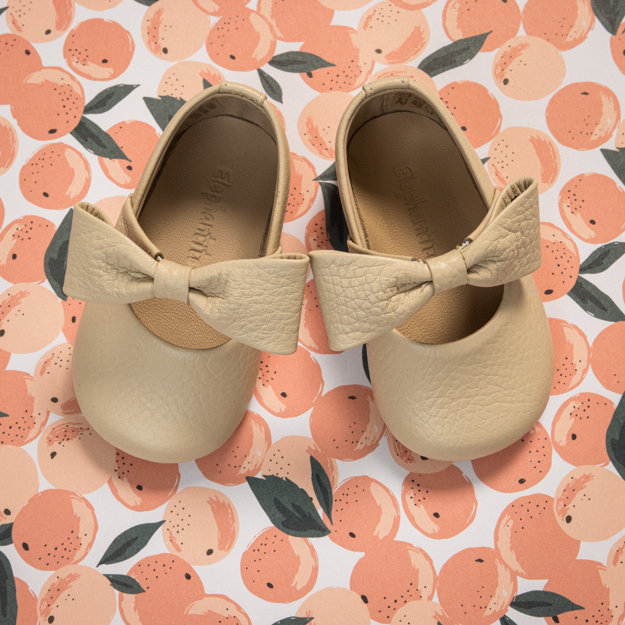 Cream-colored baby ballerina shoes with textured large bows on top and round toes.