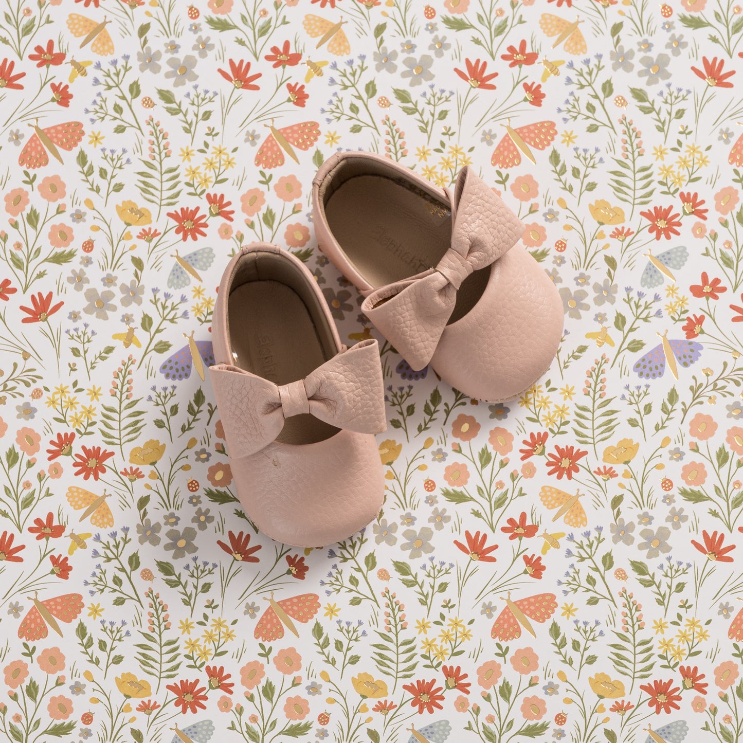 Soft pink baby ballerina shoes with large textured bows on top, made from smooth material.